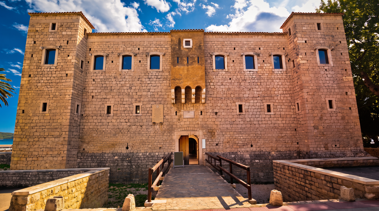 Vitturi Castle in Kaštela: a broad stone keep with corner towers and a small balcony over the door, reached by a bridge across the old moat.